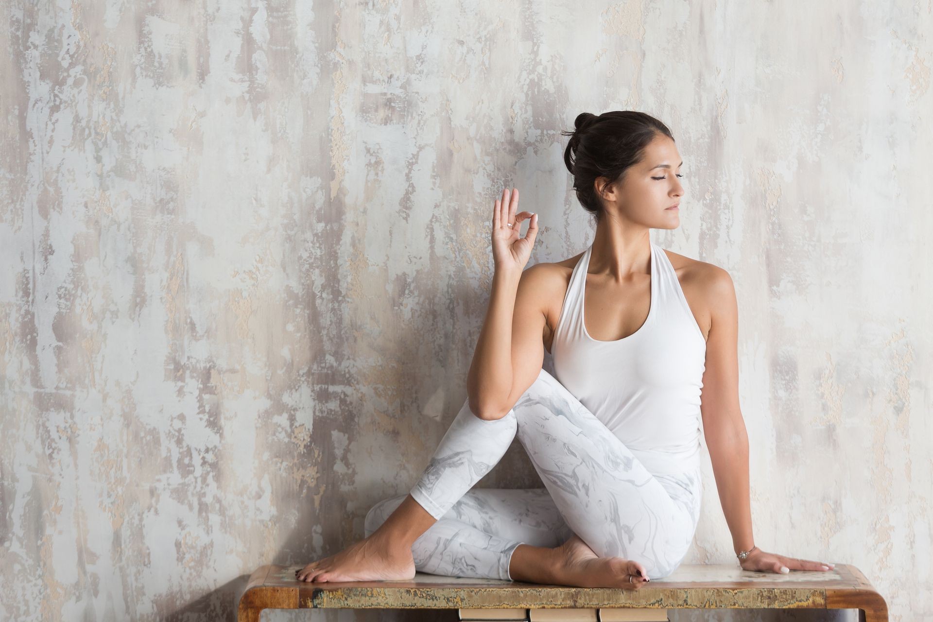 Slim beautiful young woman yoga instructor doing asana sitting on a vintage console against the background of a concrete wall. Yoga concept and take care of yourself
